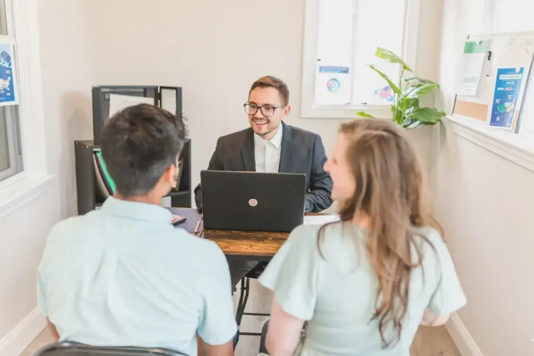 Professional man in suit and glasses smiling at couple during office meeting.