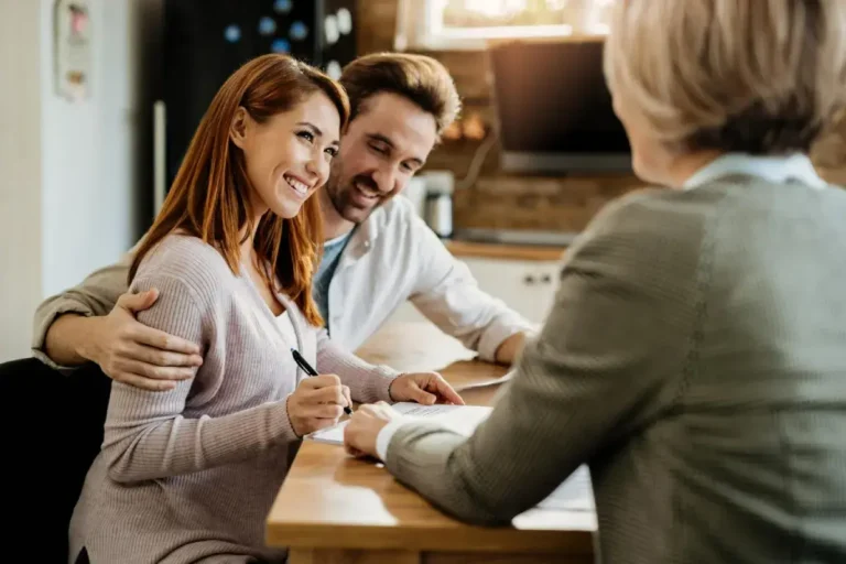 Smiling couple signing documents at a wooden table with a professional woman.