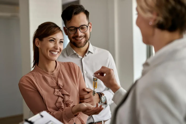 Smiling couple receiving house keys from a real estate agent indoors.