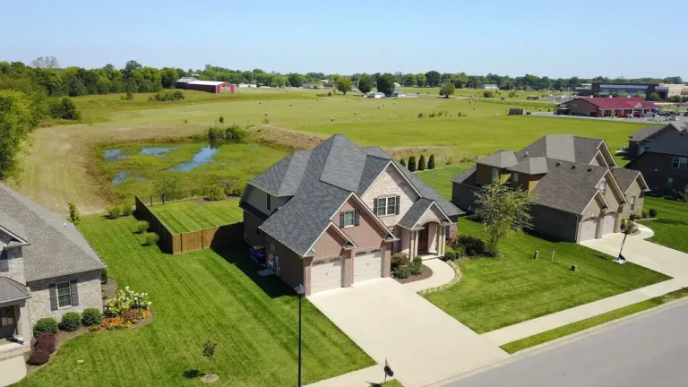 Aerial view of suburban houses with manicured lawns and a pond in the background.