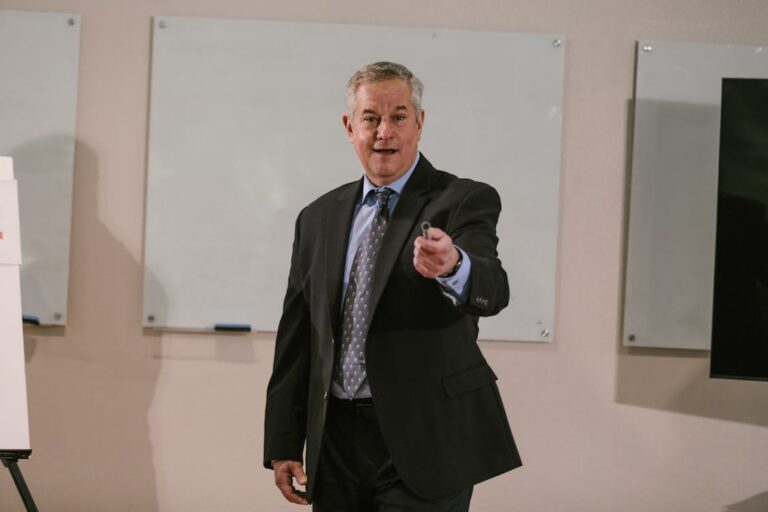 Middle-aged man in a black suit presenting in front of whiteboards.