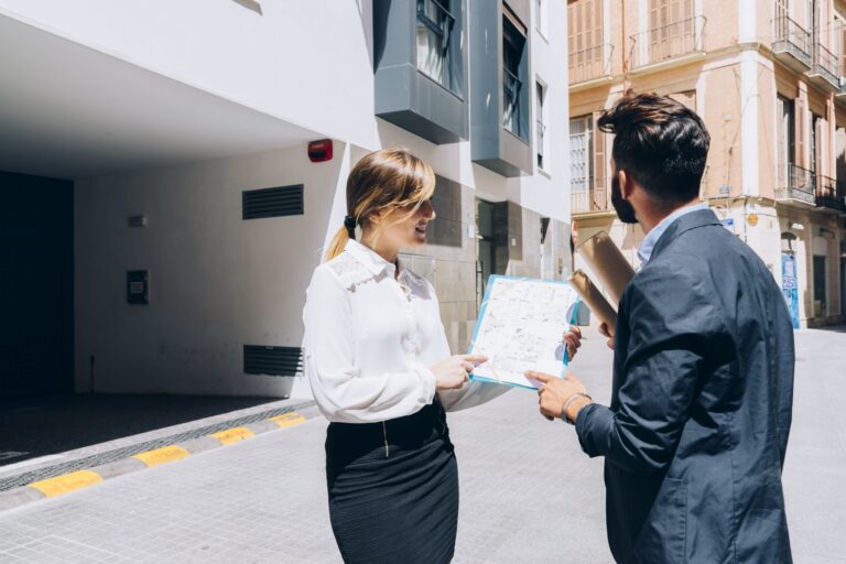 Two professionals discussing architectural plans outside a modern building on a sunny day.