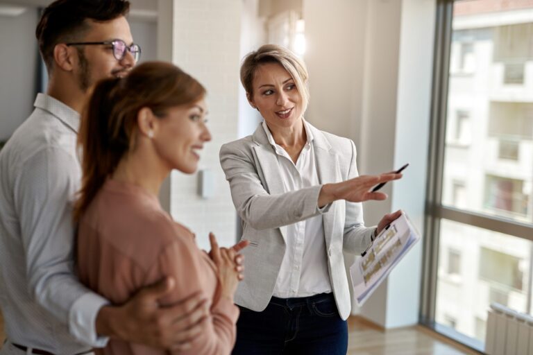Professional real estate agent showing floor plans to smiling couple in modern apartment.