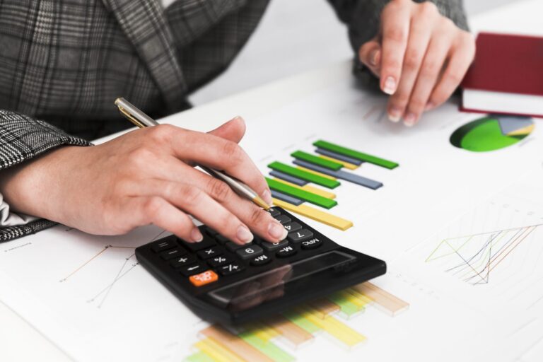 Close-up of hands using a calculator and analyzing colorful financial charts and graphs.