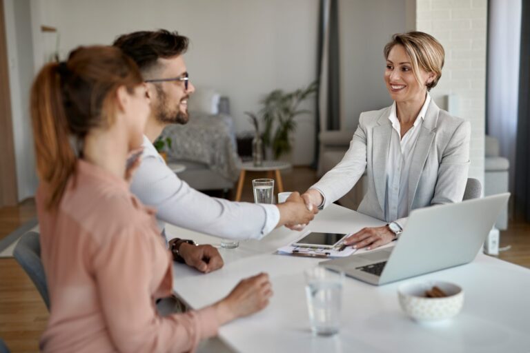Professional woman in gray suit shaking hands with man during business meeting.
