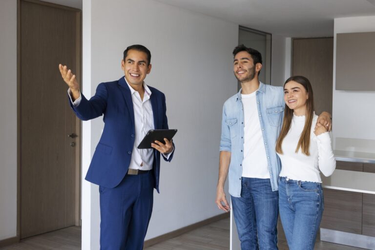 Real estate agent in blue suit showing a modern apartment to a smiling couple.