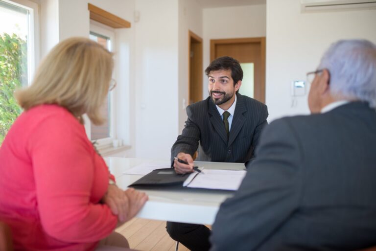Businessman in dark suit discussing documents with elderly couple at table