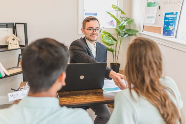 Mortgage advisor in suit shaking hands with a couple in a bright office.