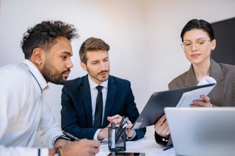 Three business professionals reviewing documents together in a modern office setting.
