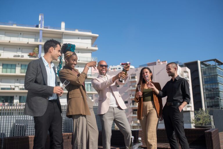 Group of five diverse professionals celebrating with champagne on a rooftop terrace.