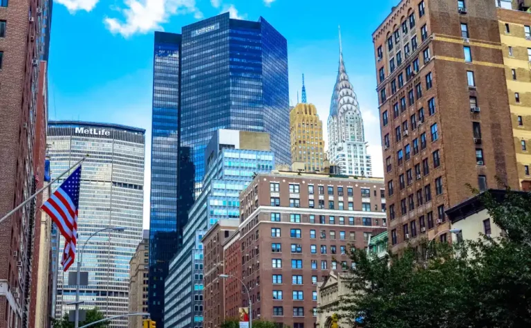 Cityscape of New York featuring MetLife and Chrysler buildings, with American flag and blue sky.