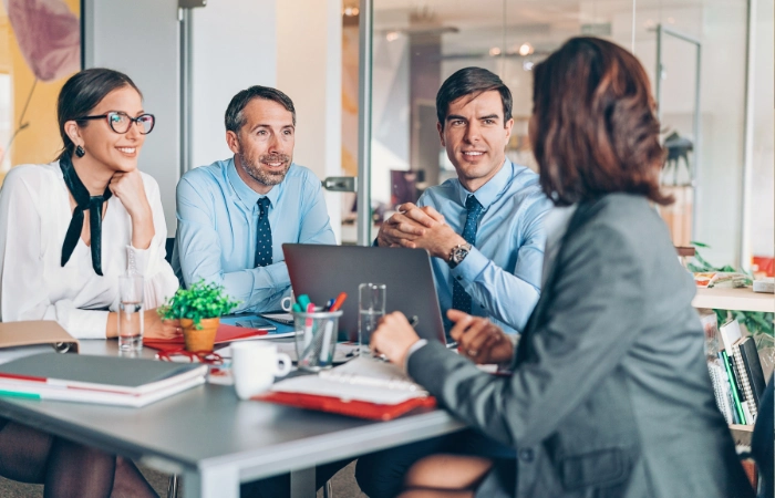 Four business professionals engaged in a meeting around a table with laptops and documents.