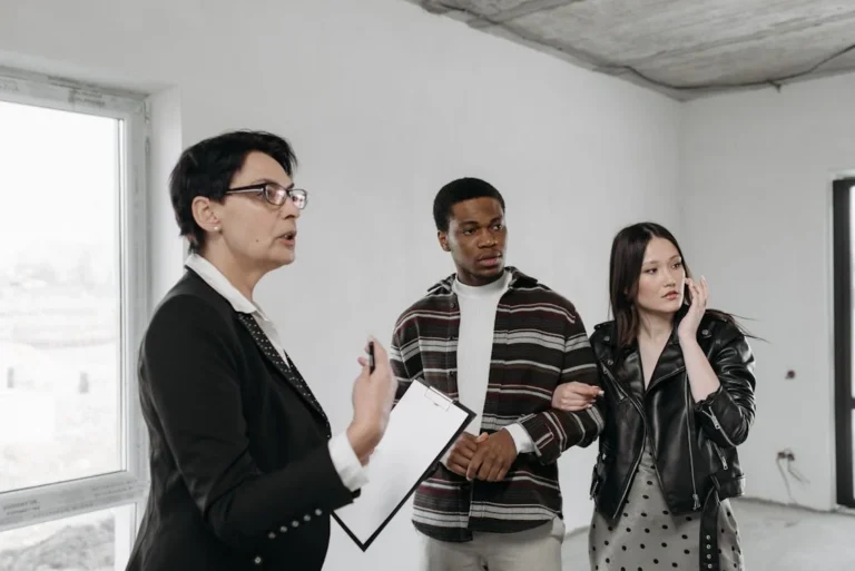Real estate agent discussing property details with a young couple inside an unfinished room.