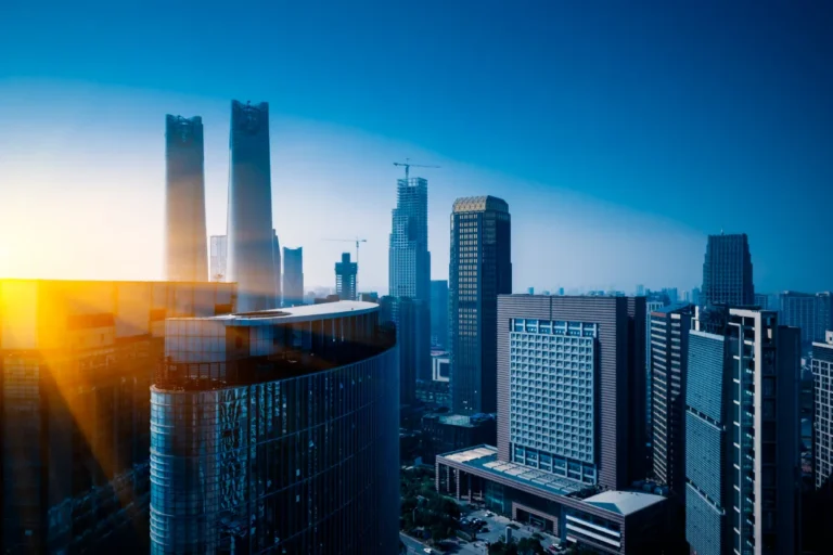 Cityscape of modern skyscrapers with sunlight reflecting off glass buildings under a clear blue sky.