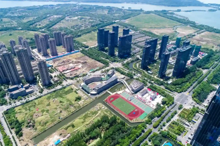 Aerial view of urban area with high-rise buildings, sports field, roads, and green spaces.