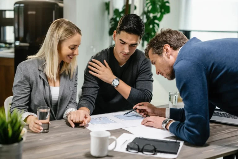 Three professionals, two men and one woman, discussing architectural plans at a table.