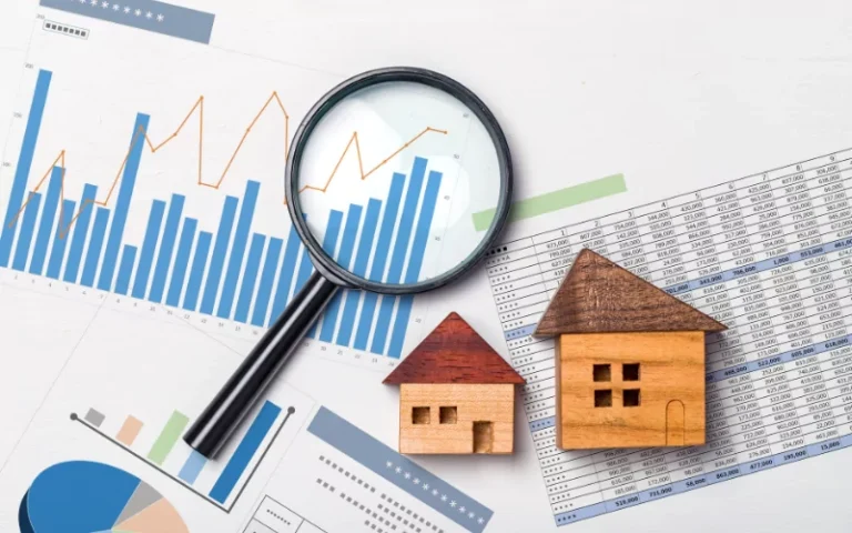 Magnifying glass over financial charts and wooden house models on white surface.