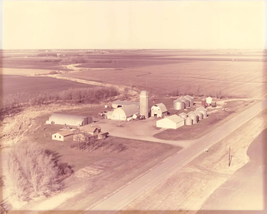 Aerial view of a rural farmstead with multiple silos, barns, and outbuildings surrounded by expansive farmland.