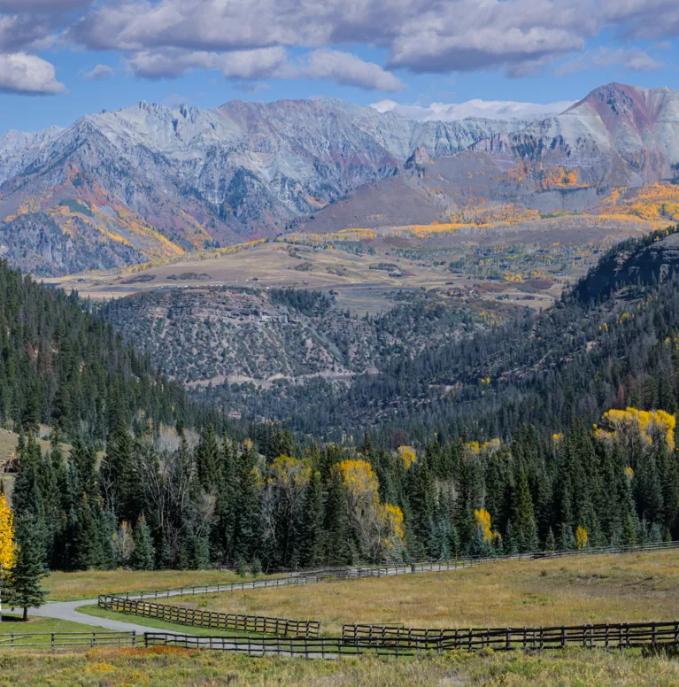 Scenic autumn mountain landscape with winding road, evergreen trees, and colorful foliage.