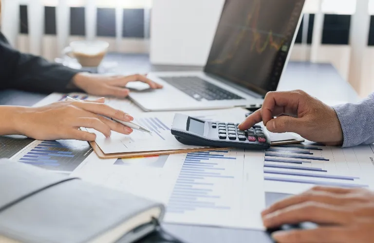 Two people working with financial documents, a calculator, and a laptop on a white desk.