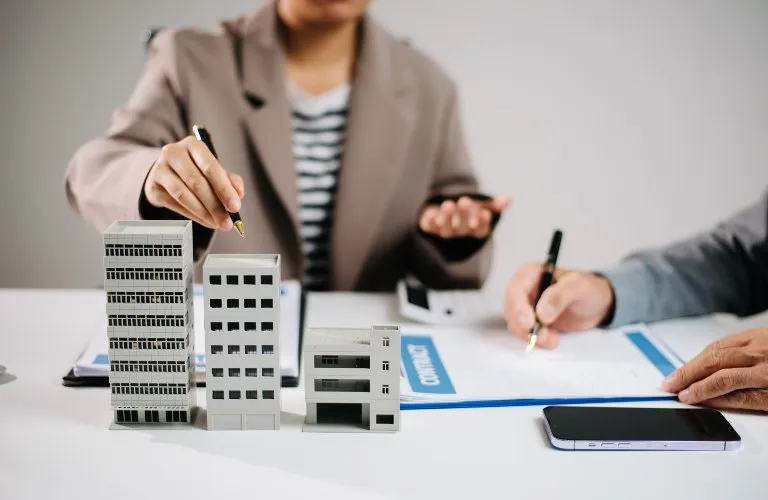 Two professionals discussing real estate with building models and contract documents on table.