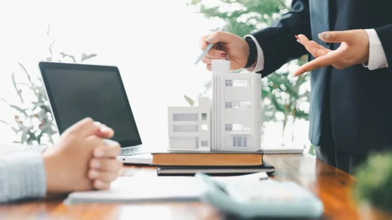 Two professionals discussing a white architectural building model on a wooden table.
