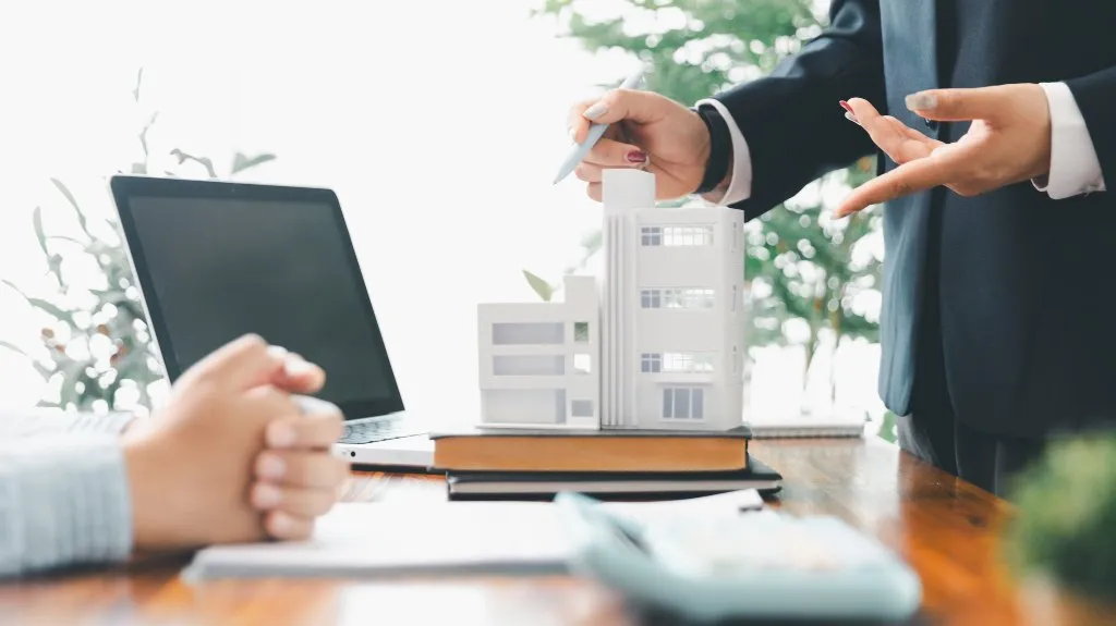 Two professionals discussing a white architectural building model on a wooden table.