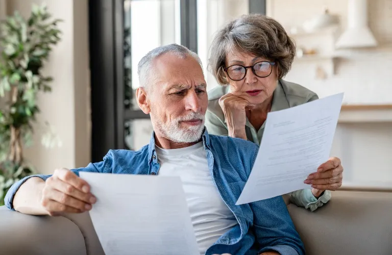 Mature man and woman seated on sofa, attentively reviewing documents together.