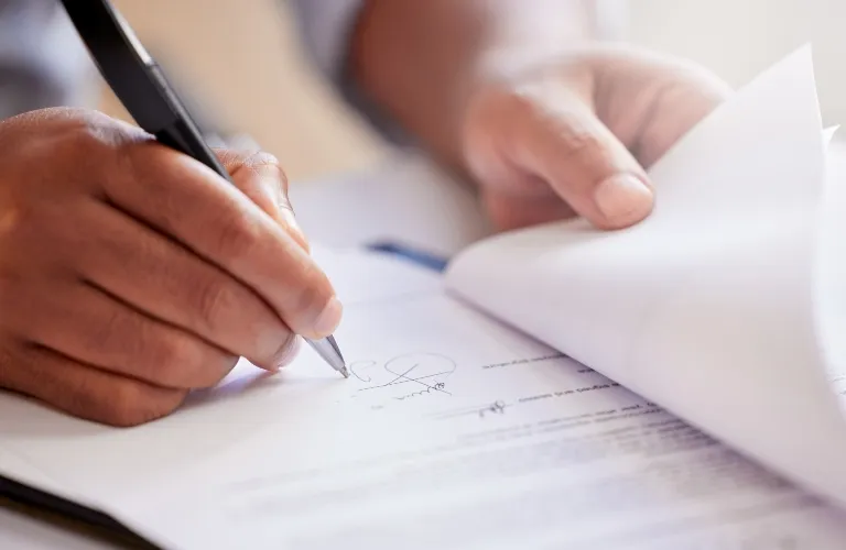 Close-up of a person signing a document with a pen, turning a page.