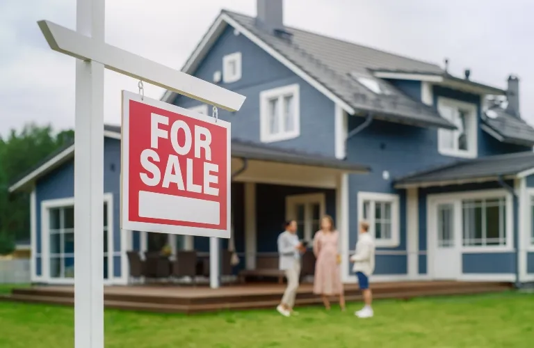 Red and white "For Sale" sign in front of a blue two-story house with three people conversing on the lawn.