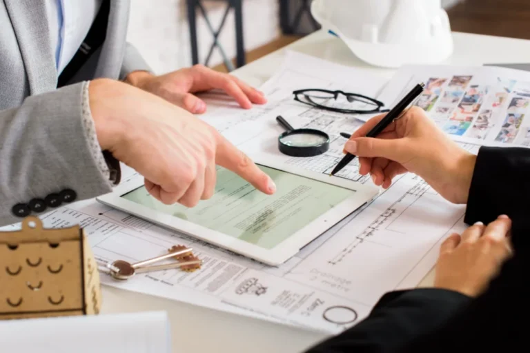 Two professionals reviewing architectural plans and documents on a tablet and paper.