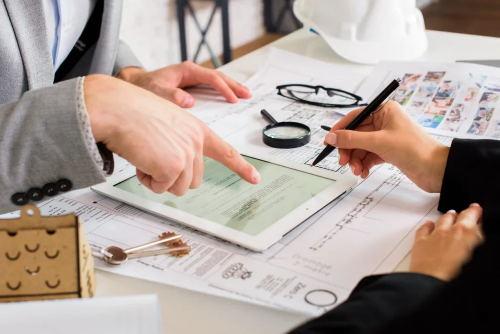 Two professionals reviewing architectural plans and documents on a tablet and paper.